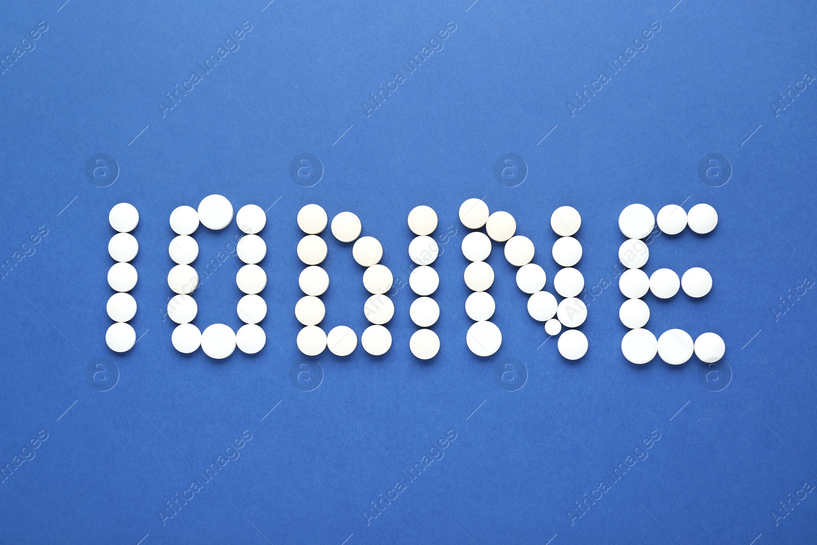 Photo of Word Iodine made of pills on blue background, flat lay