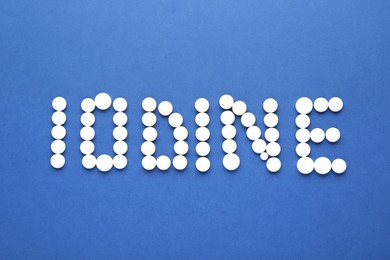 Word Iodine made of pills on blue background, flat lay