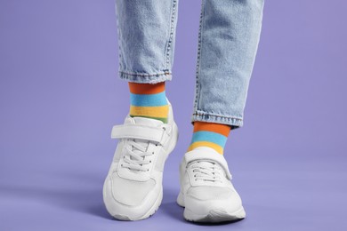Photo of Woman in stylish colorful socks, sneakers and jeans on violet background, closeup
