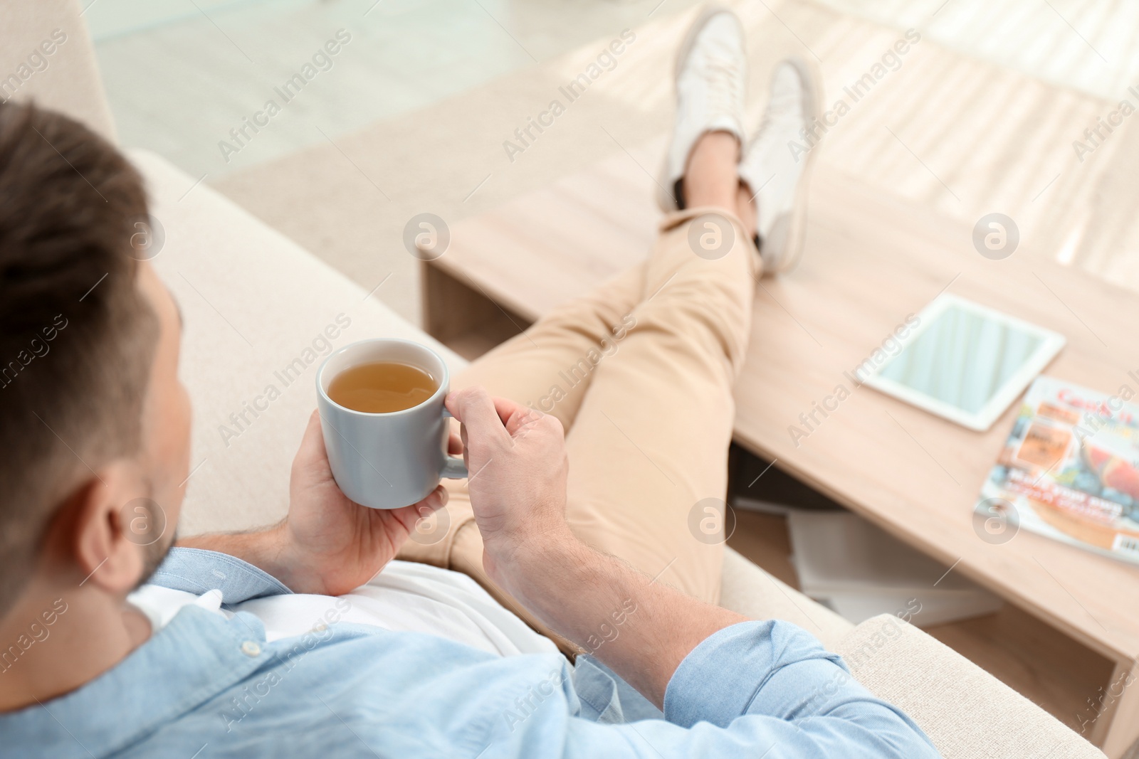 Photo of Man with cup of hot tea relaxing on sofa at home, closeup. Space for text