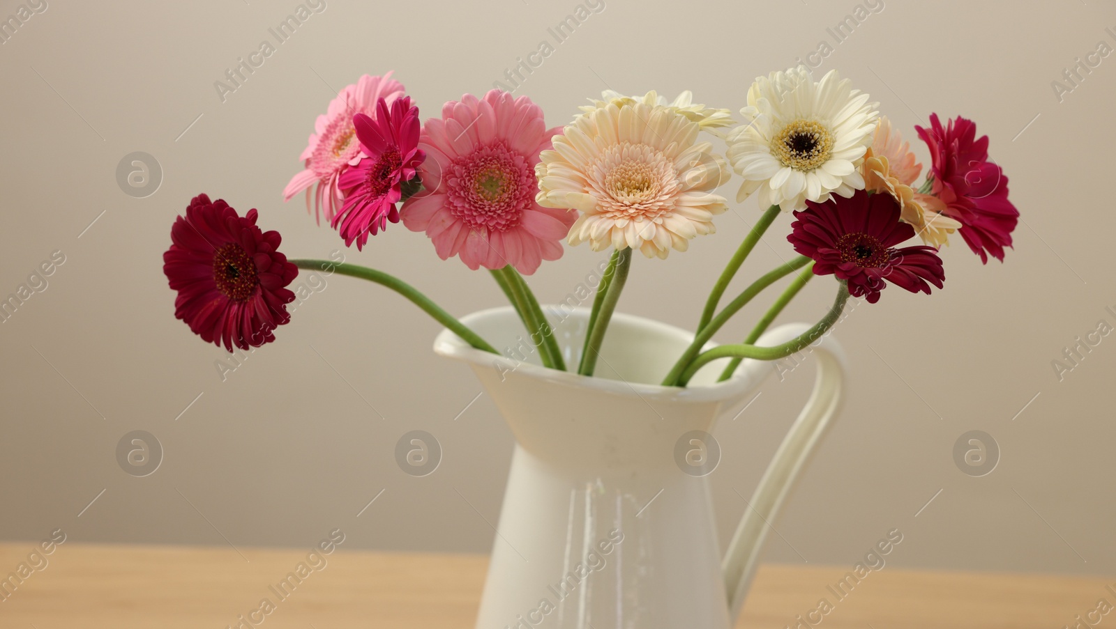 Photo of Jug with beautiful gerbera flowers on wooden table