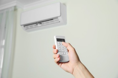 Man operating air conditioner with remote control indoors, closeup