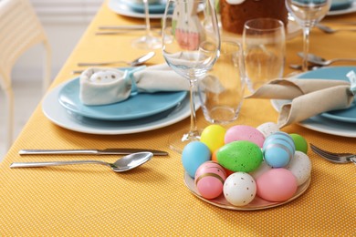 Photo of Festive table setting with painted eggs, glasses and cutlery. Easter celebration