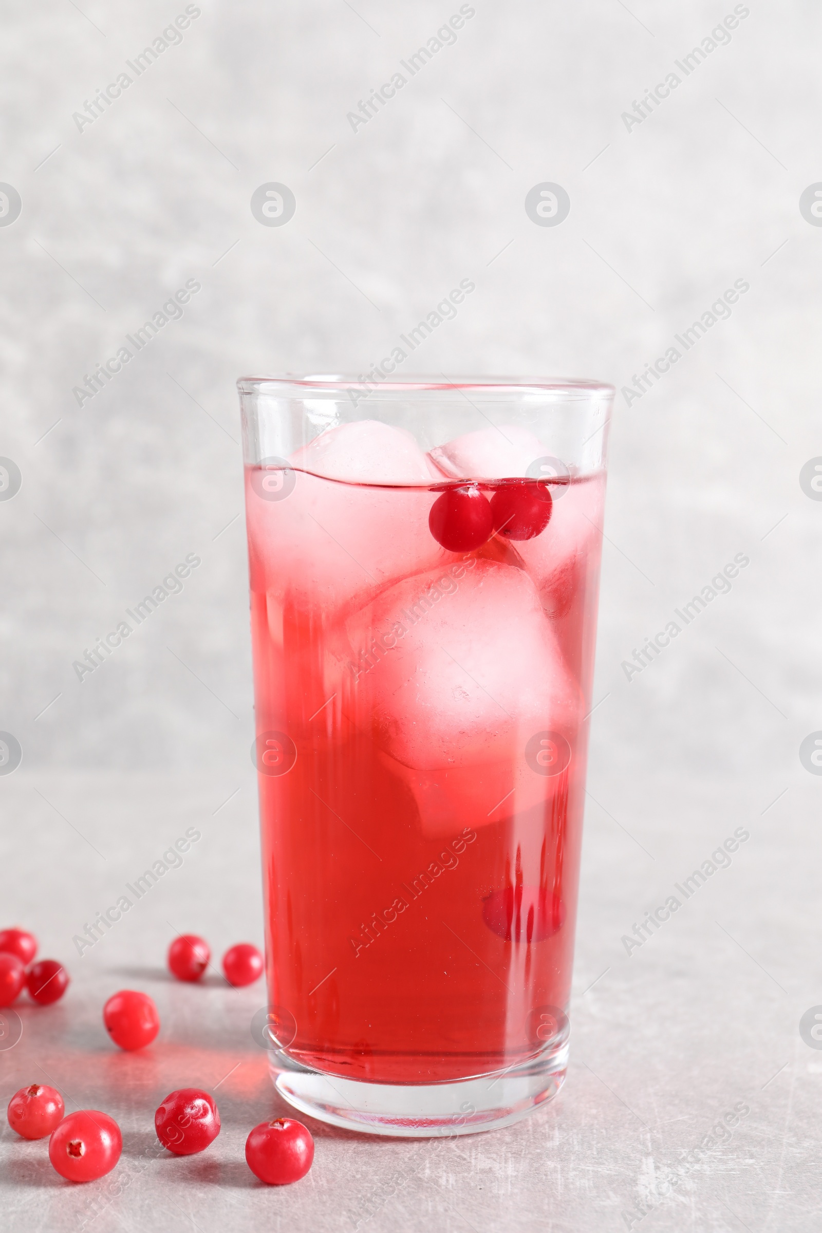 Photo of Tasty cranberry juice with ice cubes in glass and fresh berries on light grey table