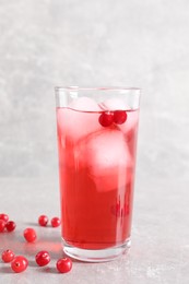 Tasty cranberry juice with ice cubes in glass and fresh berries on light grey table