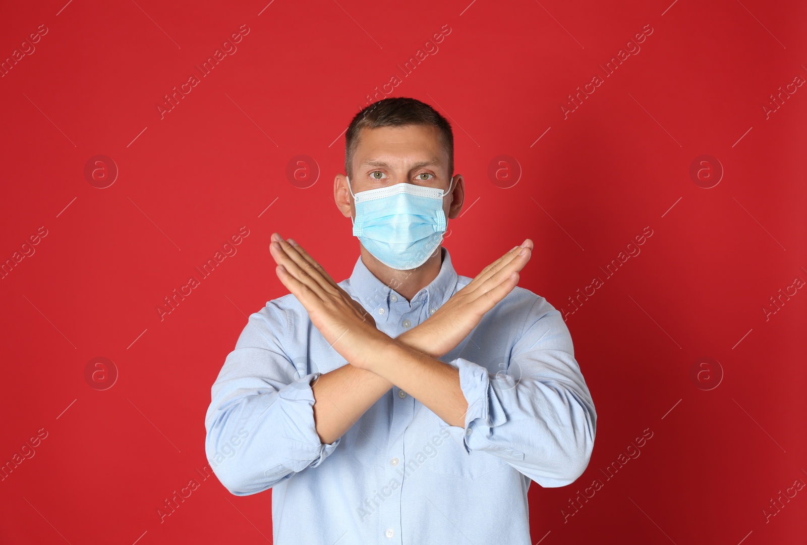 Photo of Man in protective mask showing stop gesture on red background. Prevent spreading of coronavirus