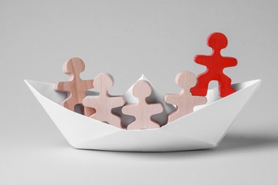 Photo of Red figure among wooden ones in paper boat on white background. Recruiter searching employee