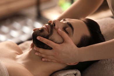 Photo of Young man receiving facial massage in beauty salon