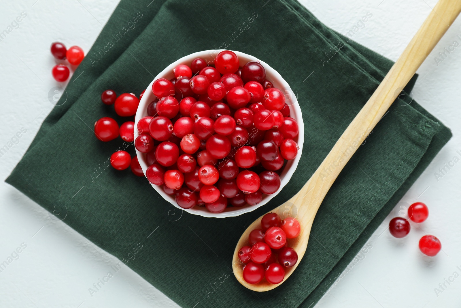 Photo of Cranberries in bowl and spoon on white table, top view