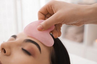 Young woman receiving facial massage with gua sha tool in beauty salon, closeup
