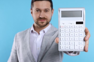 Photo of Happy accountant with calculator on light blue background, selective focus