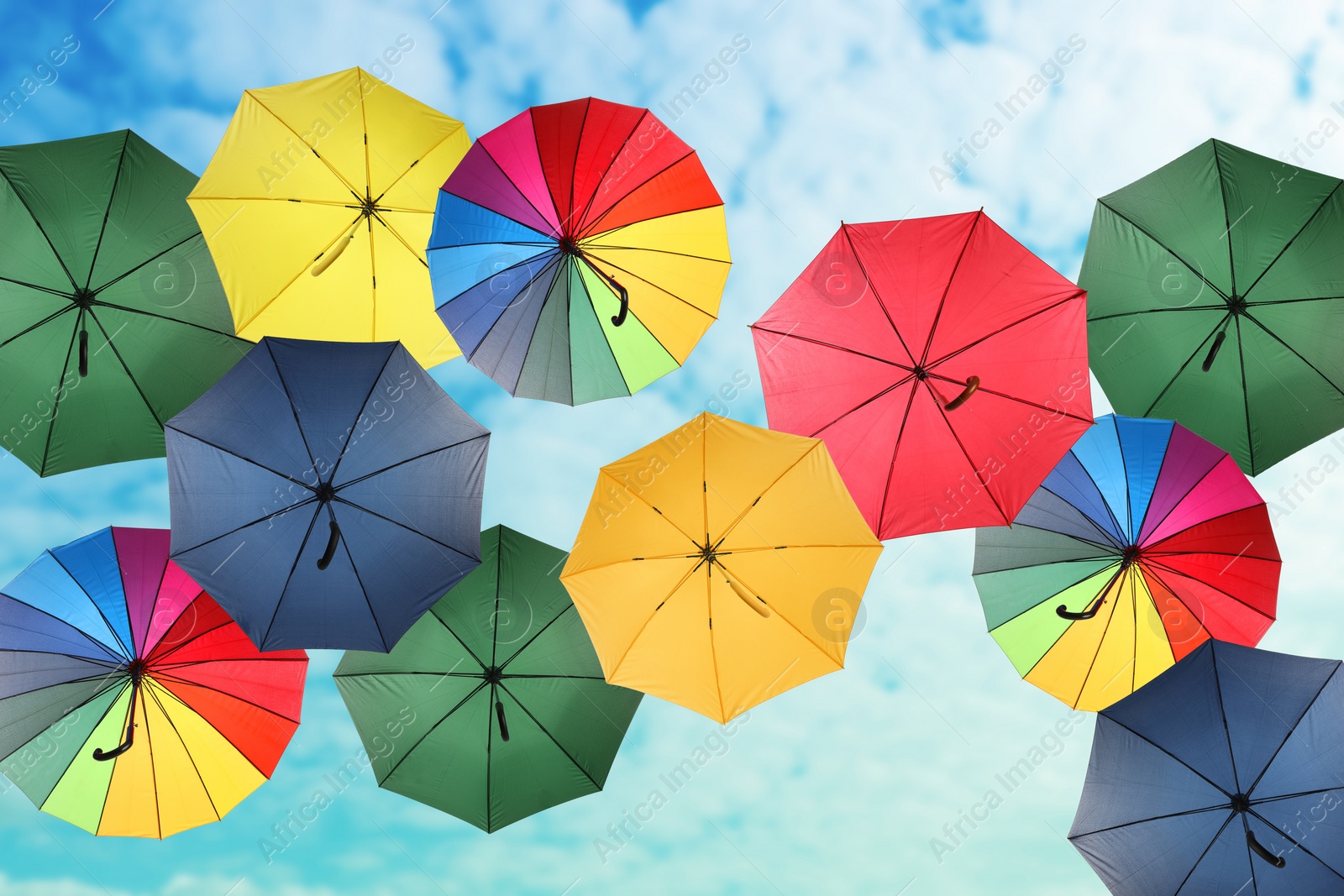 Image of Group of different colorful umbrellas against blue sky with white clouds on sunny day, bottom view