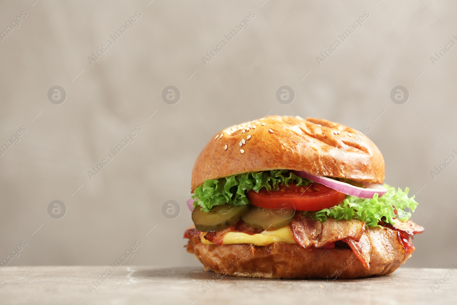 Photo of Delicious burger with bacon on table against grey background. Space for text