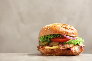 Photo of Delicious burger with bacon on table against grey background. Space for text