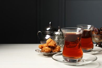 Glasses of tea, baklava and date fruits served in vintage tea set on white wooden table, space for text