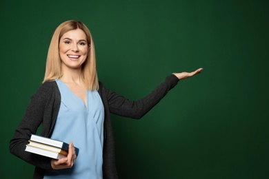 Beautiful teacher with books pointing at chalkboard, space for text