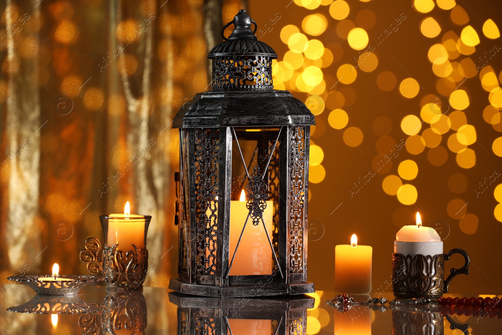 Photo of Arabic lantern and burning candles on mirror surface against blurred lights