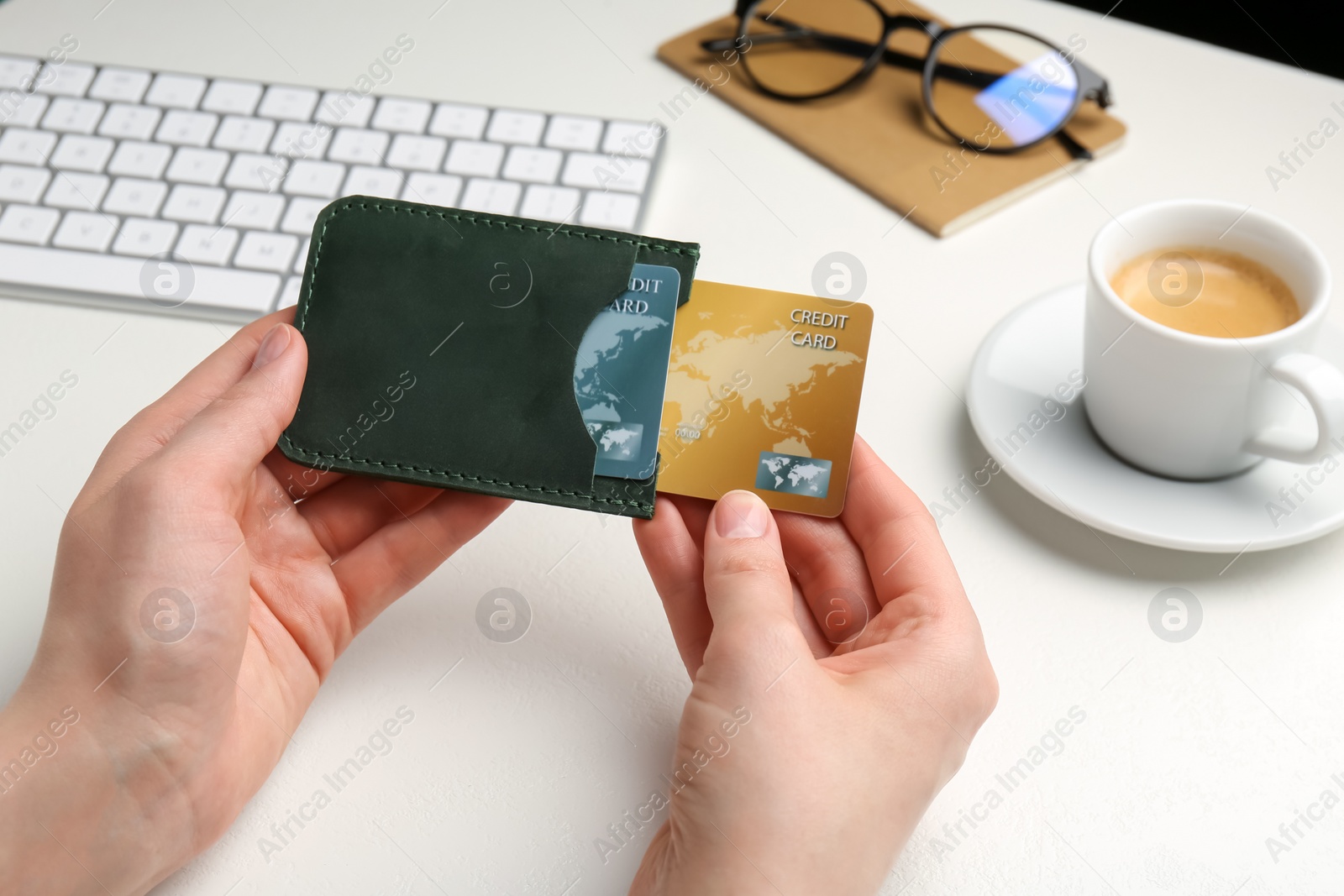 Photo of Woman holding leather card holder with credit cards at white table, closeup