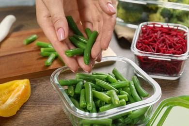 Photo of Woman putting green beans into glass container at wooden table, closeup. Food storage