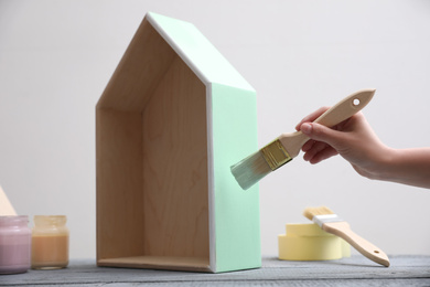 Photo of Woman painting wooden house model at grey table, closeup