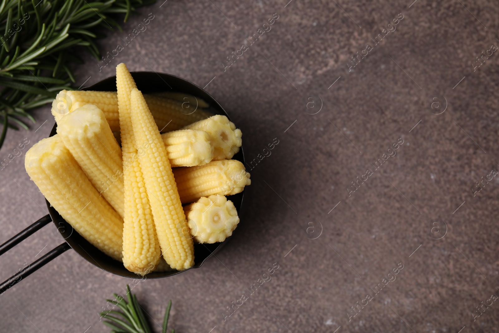 Photo of Tasty fresh yellow baby corns in dish on brown table, top view. Space for text