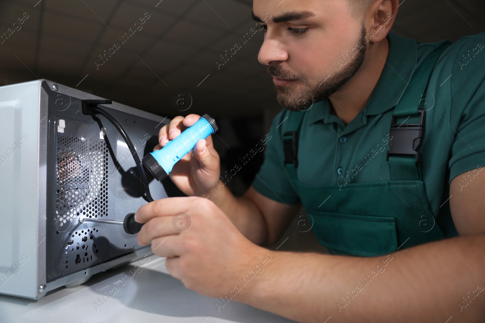 Photo of Repairman with flashlight fixing microwave oven indoors, closeup