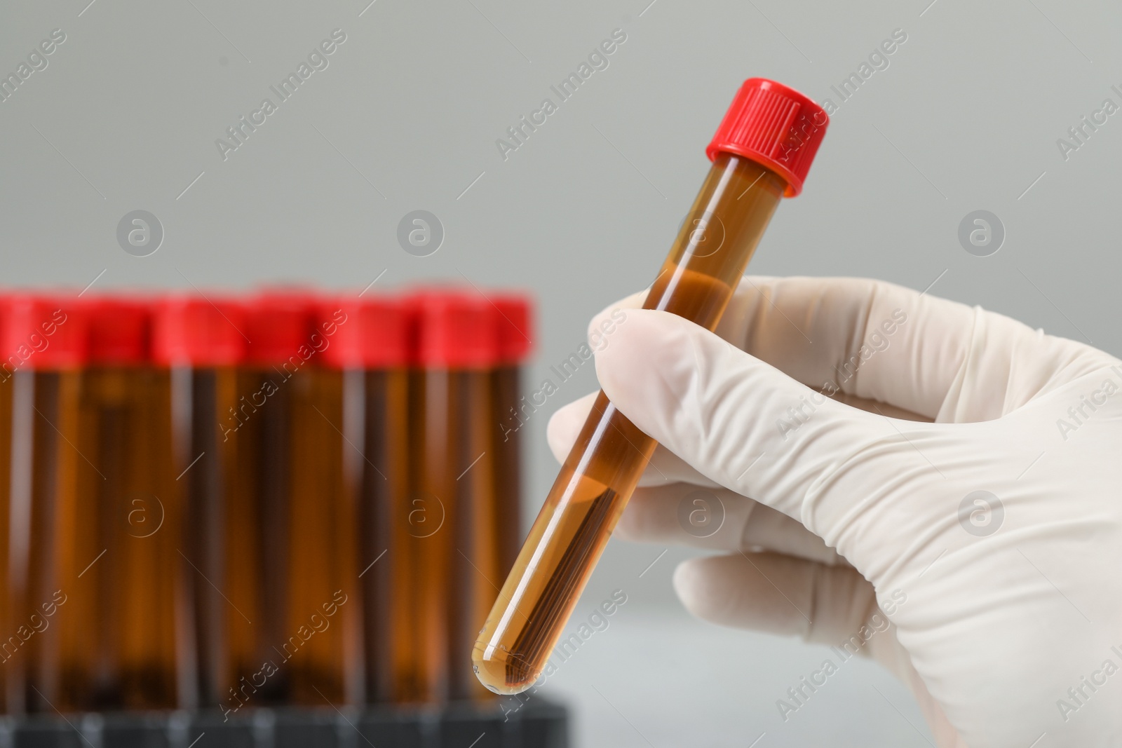 Photo of Scientist holding test tube with brown liquid against light background, closeup. Space for text