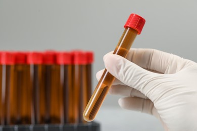Photo of Scientist holding test tube with brown liquid against light background, closeup. Space for text
