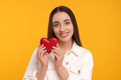 Happy young woman holding decorative red heart on yellow background