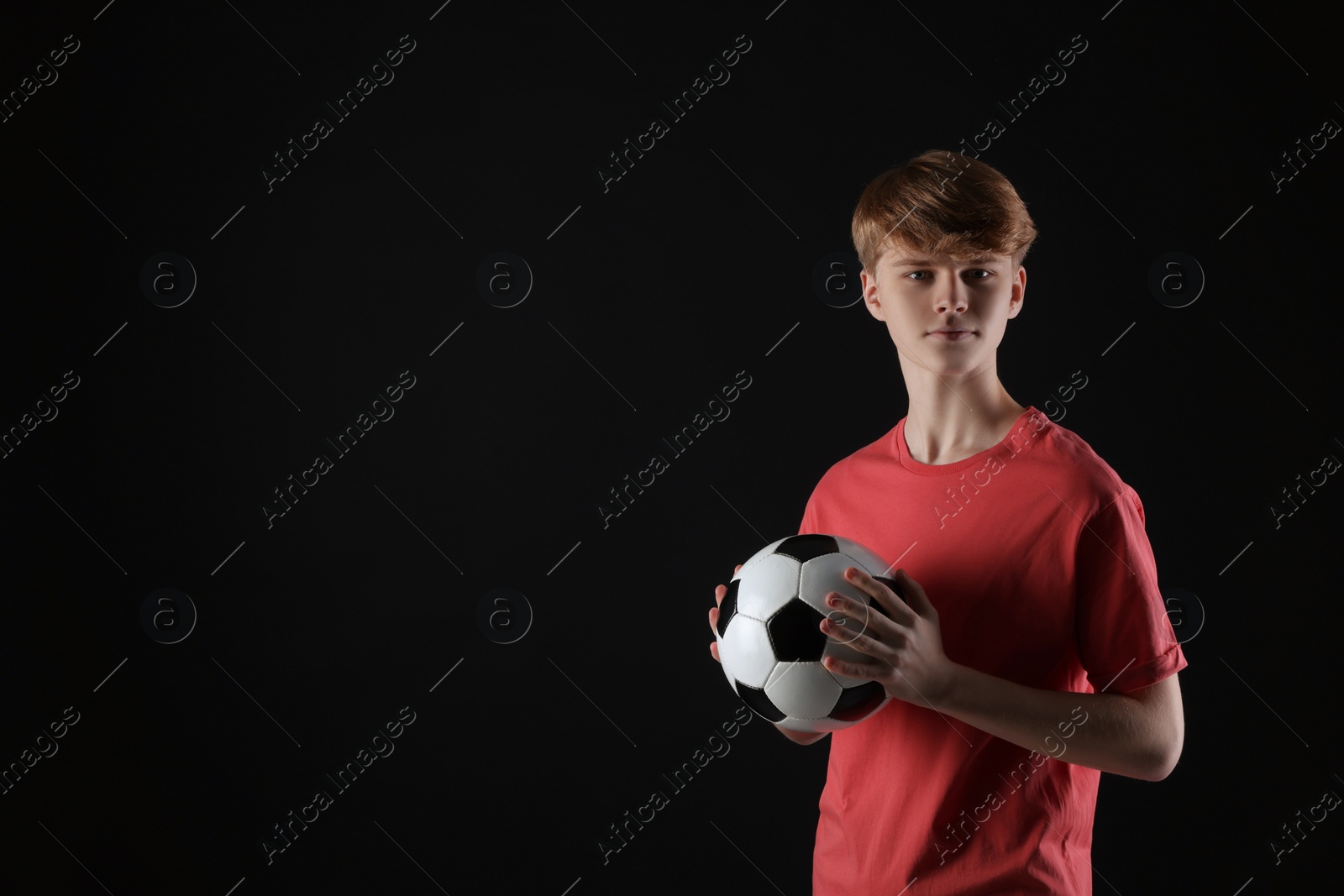 Photo of Teenage boy with soccer ball on black background. Space for text