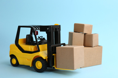 Forklift model and carton boxes on light blue background. Courier service