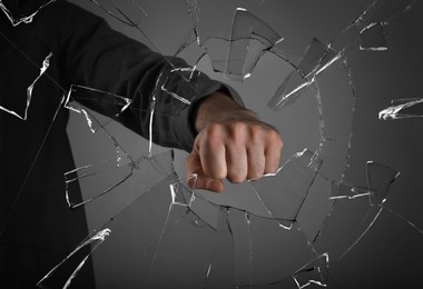 Image of Man breaking window with fist on grey background, closeup