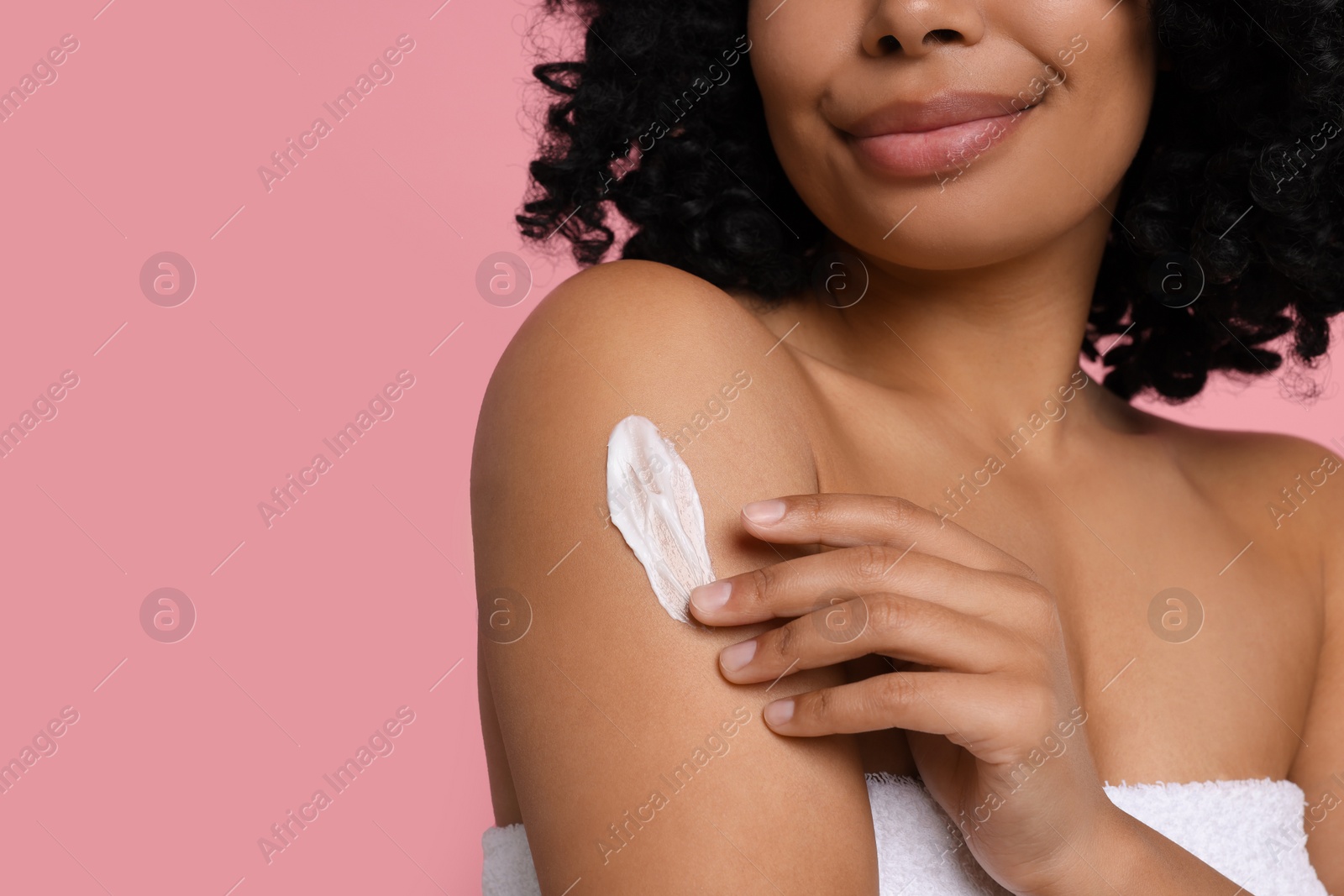 Photo of Young woman applying body cream onto shoulder on pink background, closeup. Space for text