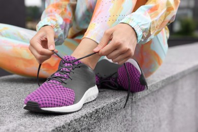 Woman in gym clothes tying shoelace of sneakers on street, closeup