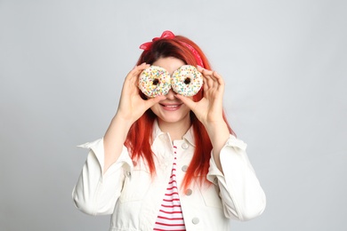 Photo of Young woman with bright dyed hair holding donuts near eyes on grey background