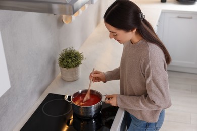 Photo of Beautiful woman with wooden spoon cooking tomato soup in kitchen, above view. Space for text