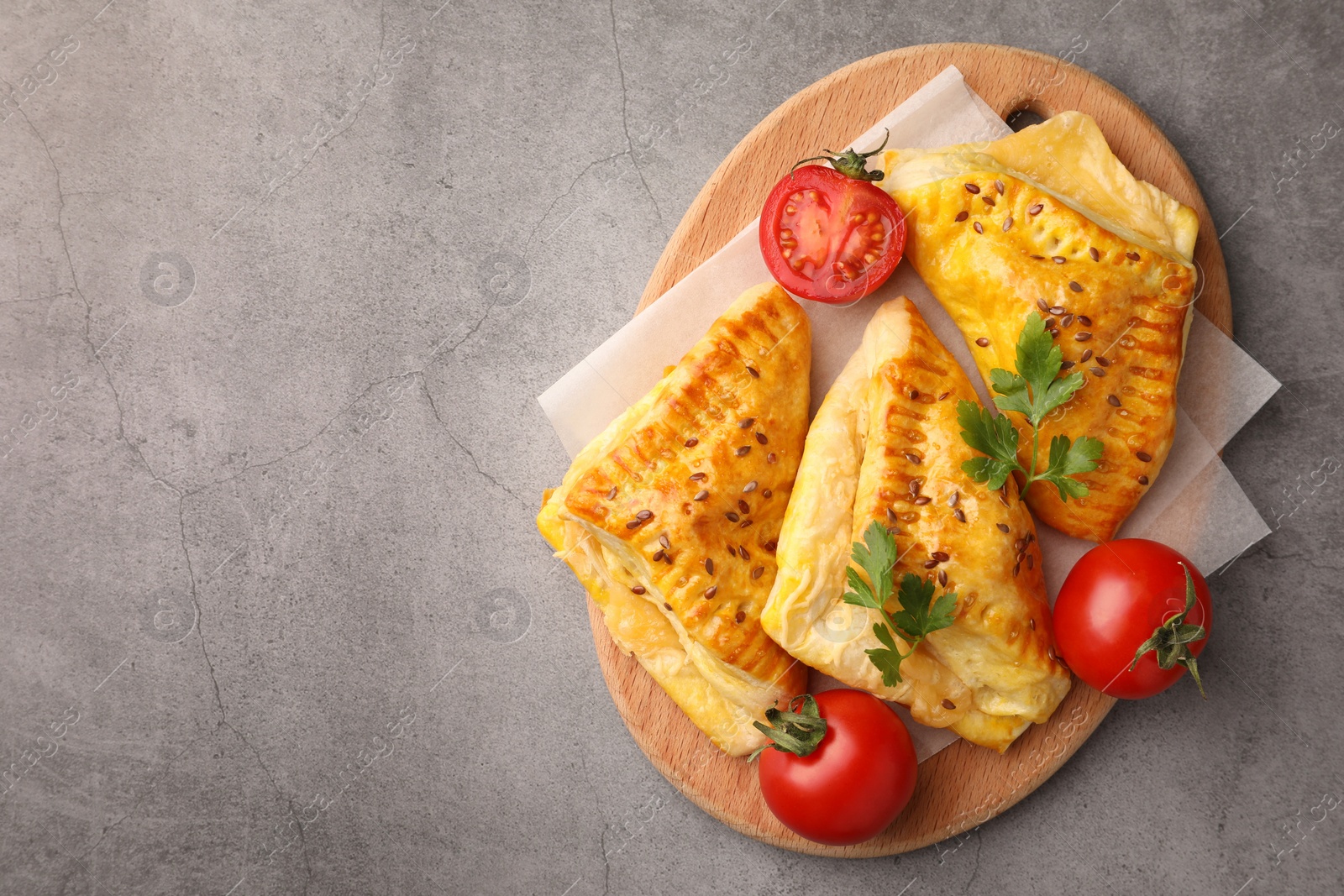 Photo of Fresh delicious puff pastry with cheese, tomatoes and parsley on grey table, top view. Space for text