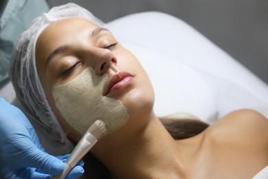 Photo of Cosmetologist applying mask on client's face in spa salon