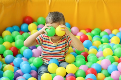 Photo of Cute little child playing in ball pit at indoor amusement park