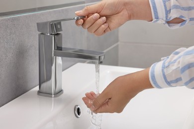 Photo of Woman washing hands with water from tap in bathroom, closeup