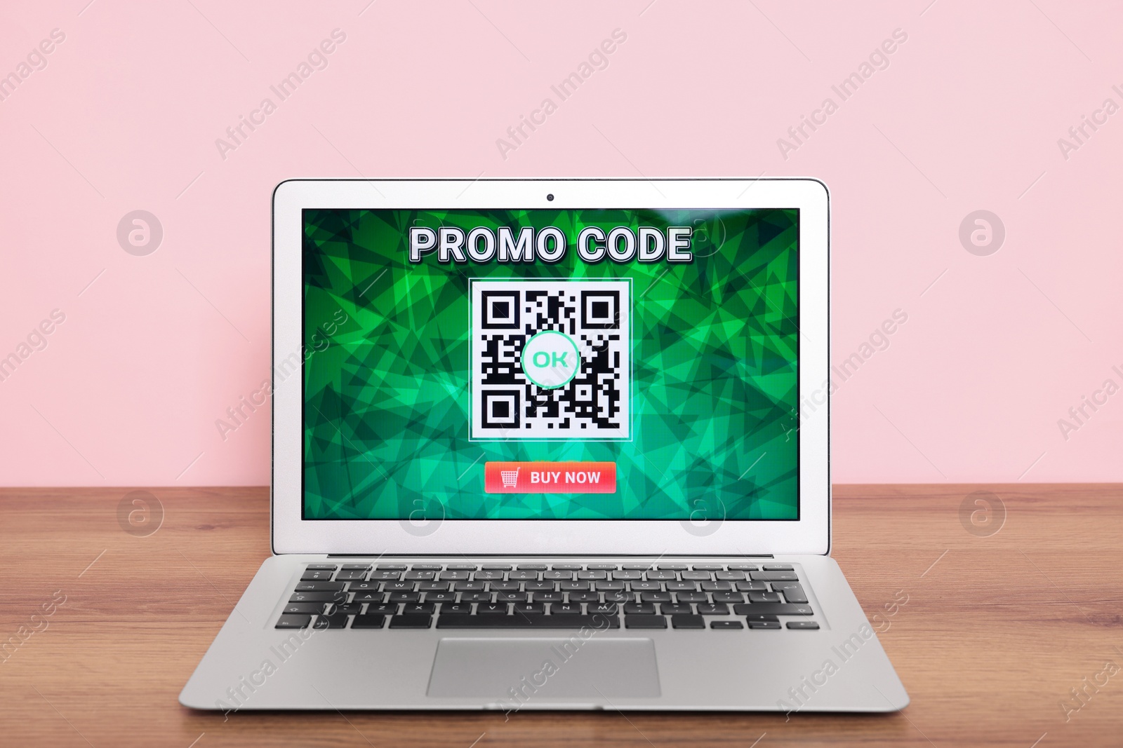 Photo of Laptop with activated promo code on wooden table near pink wall