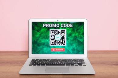 Laptop with activated promo code on wooden table near pink wall