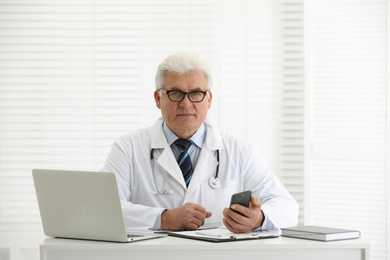 Photo of Senior doctor with smartphone at table in office