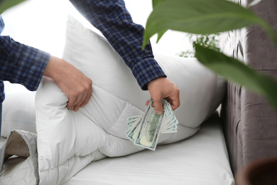 Man hiding dollar banknotes under blanket in bedroom, closeup. Money savings