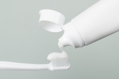 Applying paste on toothbrush against grey background, closeup