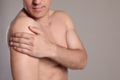 Man suffering from shoulder pain on beige background, closeup