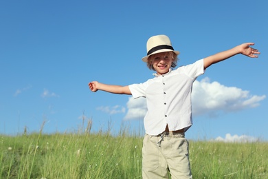 Photo of Cute little boy wearing stylish hat outdoors. Child spending time in nature