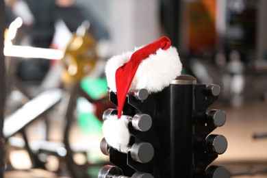 Photo of Santa Claus hat on stand with dumbbells in gym