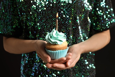 Woman holding delicious birthday cupcake with burning candle, closeup