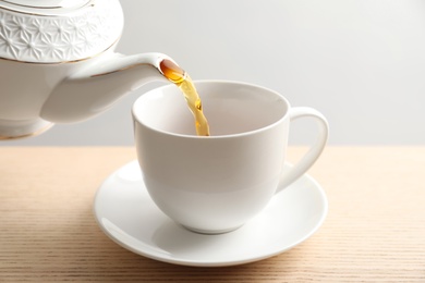 Pouring hot tea into porcelain cup on wooden table